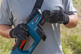 A person wearing safety equipment inserts a battery into a cordless brushcutter.