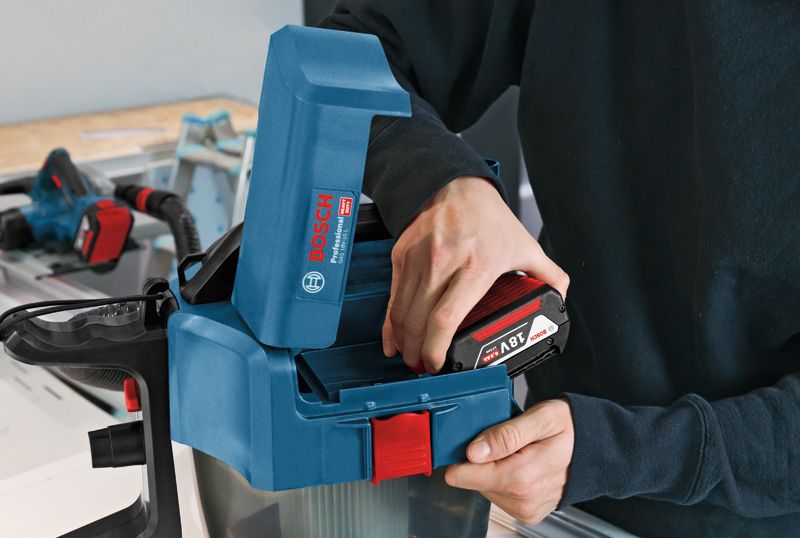 GAS 18V-10 L Person inserts a battery into a blue power tool on a workbench.