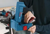 Person inserts a battery into a blue power tool on a workbench.
