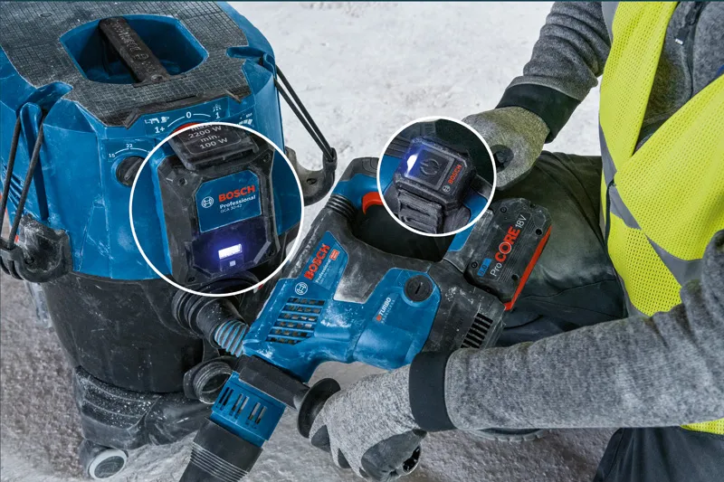 A person wearing safety equipment uses a power tool connected to a dust extractor system.
