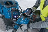 A person wearing safety equipment uses a power tool connected to a dust extractor system.