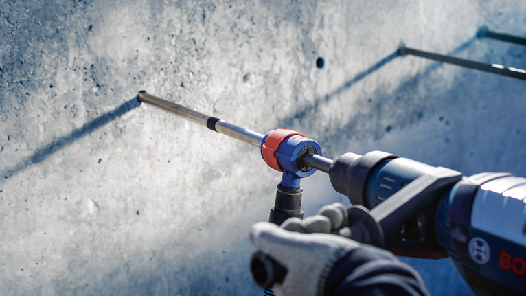 Person wearing safety equipment drills into a concrete wall.