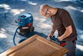 A person wearing safety equipment sands a wooden door with a power planer.