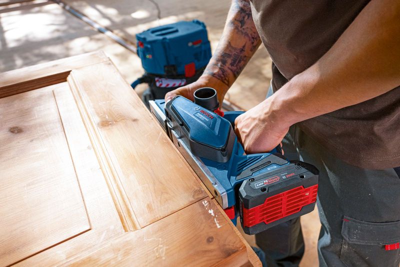 A person smooths the edge of a wooden door using a cordless planer.