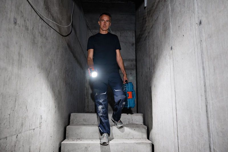 A person holds a cordless work light and tool case while descending concrete stairs.