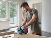 Person wearing safety equipment trims wooden board with a cordless circular saw.