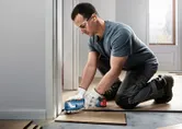 A person wearing safety equipment trims wooden flooring with a cordless multi-tool.