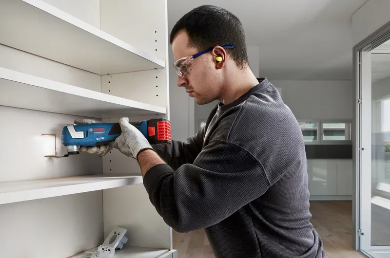 GOP 18V-34 A person wearing safety equipment cuts a shelf panel with a multi tool.