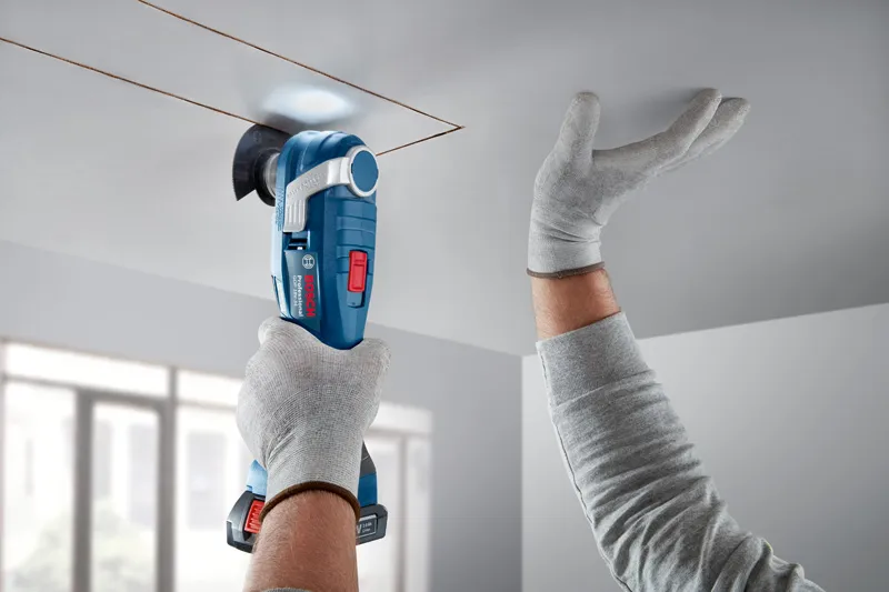 GOP 18V-34 A person wearing safety equipment cuts a ceiling panel with a cordless multi-tool.
