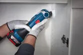 A person wearing safety equipment uses a cordless multi-tool to cut a cabinet opening.