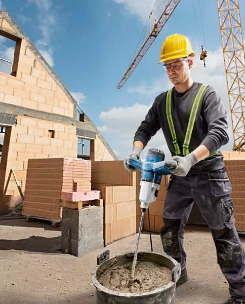 A person wearing safety equipment mixes cement with a stirring mechanism at a construction site.