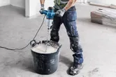 A person wearing safety equipment mixes paint with an electric stirring mechanism.