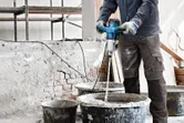 A person wearing safety equipment mixes construction material with a stirring mechanism.