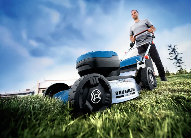 A person pushes a cordless lawnmower over grass in an outdoor area.