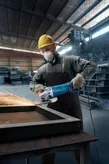 A person wearing safety equipment grinds metal, creating sparks in a factory.