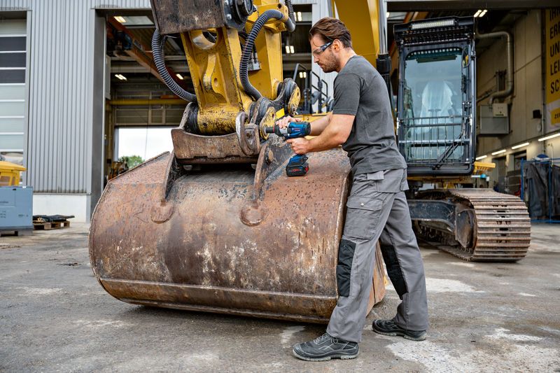 GDS 18V-1600 HC A person wearing safety equipment uses an impact wrench on heavy construction machinery.