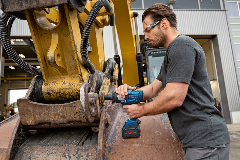 GDS 18V-1600 HC A person wearing safety equipment uses an impact wrench on heavy machinery outdoors.
