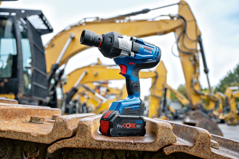 Cordless impact wrench resting on heavy machinery tracks at a construction site.