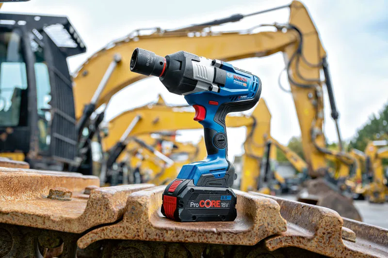 Cordless impact wrench resting on heavy machinery tracks at a construction site.