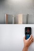A person uses a detector to scan a wall for metal, wood, and electrical wiring.