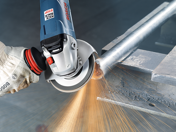 Person wearing safety equipment cuts a metal pipe with an angle grinder, producing sparks.