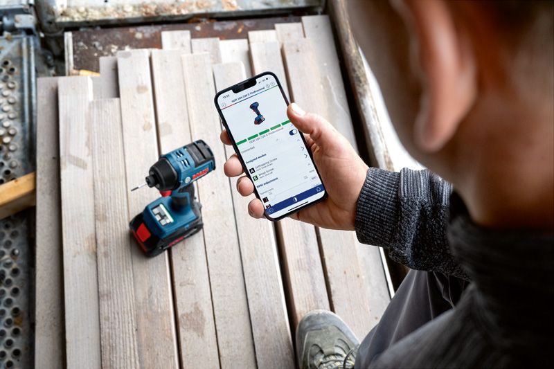 GDR 18V-220 C A person checks a power tool's app features on a smartphone near a cordless drill.