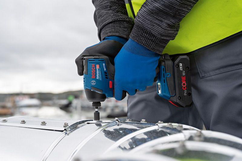 GDR 18V-220 C A person wearing safety equipment fastens a screw on metal with a cordless impact driver.