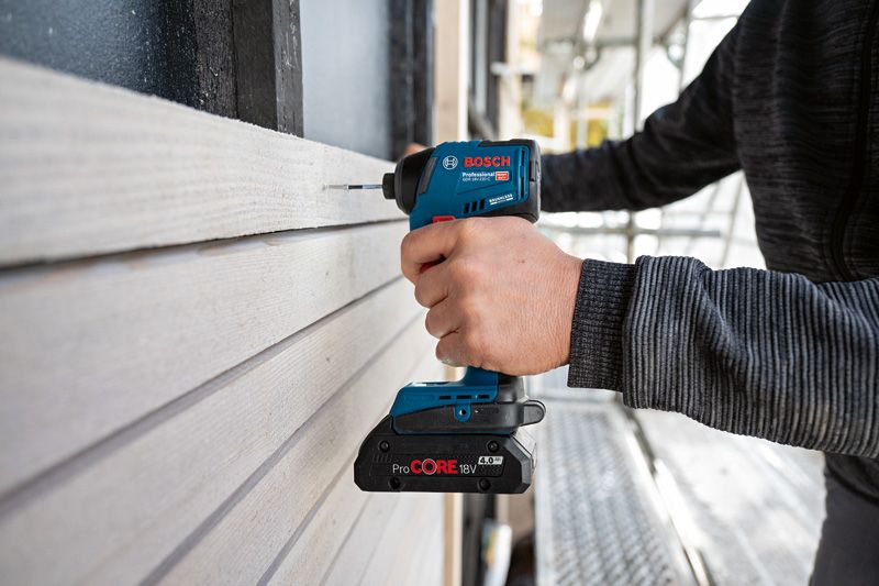 GDR 18V-220 C A person uses a cordless power drill to fasten screws into wooden siding.