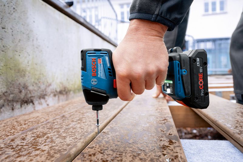 A person fastens a screw into wet wooden planks using a cordless power drill.