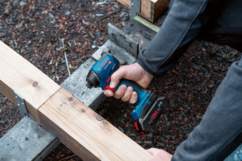 A person drives a screw into a wooden beam with a cordless impact driver.