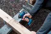 A person drives a screw into a wooden beam with a cordless impact driver.