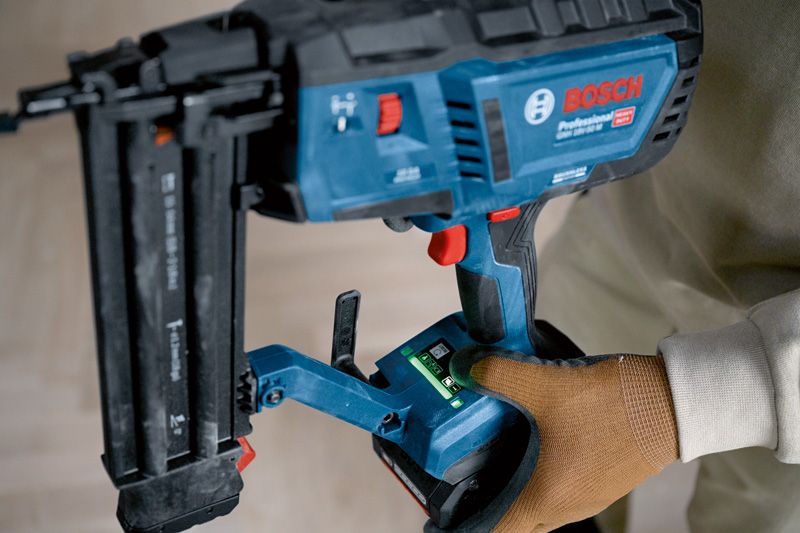 A person wearing safety equipment operates a cordless brad nailer.