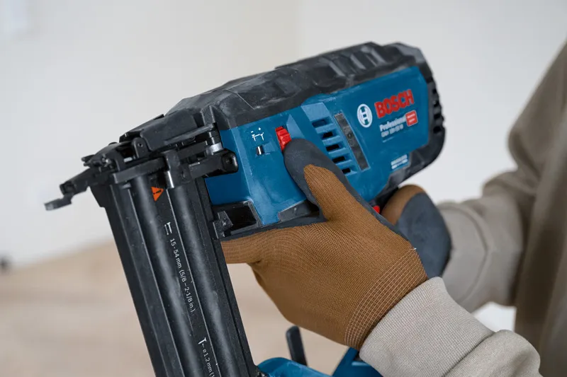 A person wearing safety equipment adjusts a cordless brad nailer.