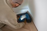 A person wearing safety equipment uses a cordless wood nailer to fasten floorboards.