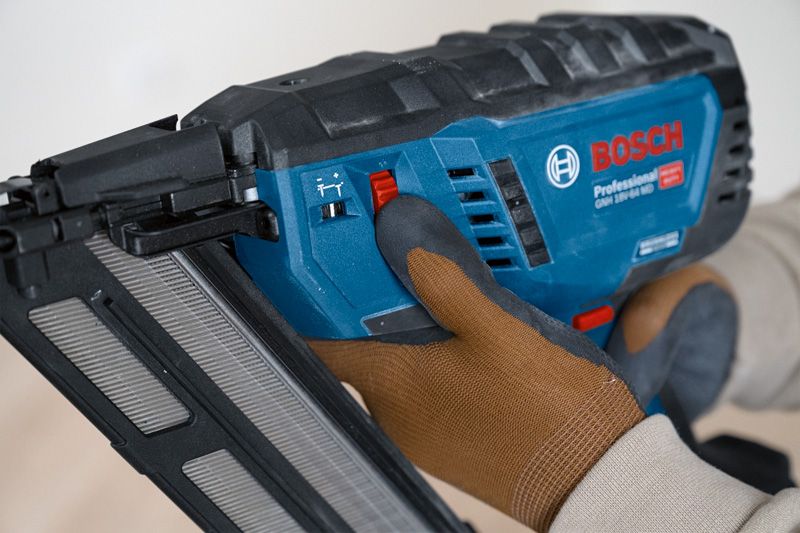 Person wearing safety equipment adjusts a cordless wood nailer.