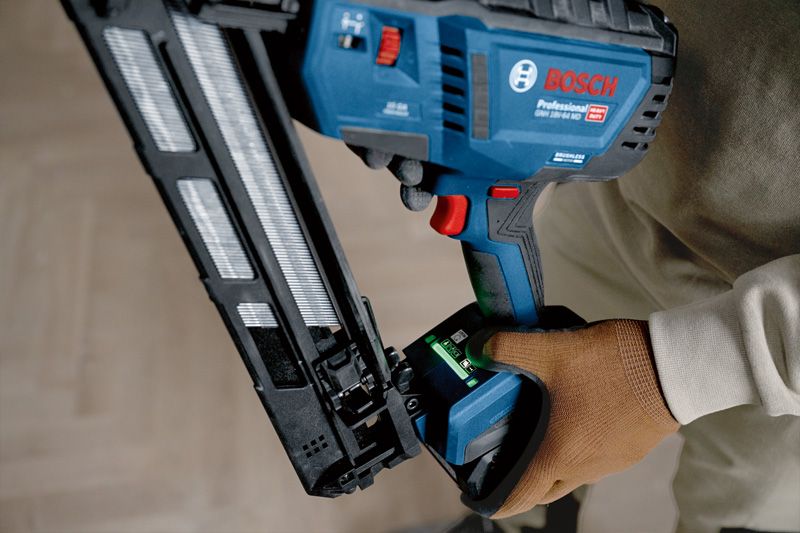 A person wearing safety equipment operates a cordless finish nailer.