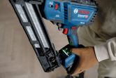 A person wearing safety equipment operates a cordless finish nailer.