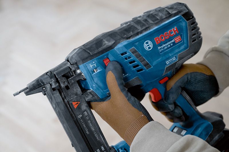 A person wearing safety equipment adjusts a cordless narrow crown stapler.