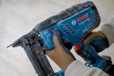 A person wearing safety equipment adjusts a cordless narrow crown stapler.