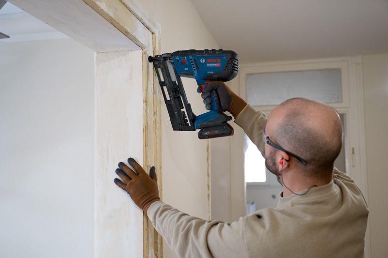 Person wearing safety equipment installing wood trim with a cordless nailer.