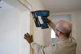 Person wearing safety equipment installing wood trim with a cordless nailer.
