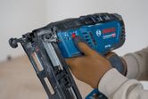 Person wearing safety equipment adjusts a cordless wood nailer.