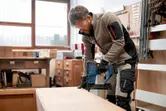 Person wearing safety equipment uses a cordless narrow crown stapler on wood.