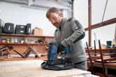 A person wearing safety equipment staples fabric to wood using a cordless wood stapler.