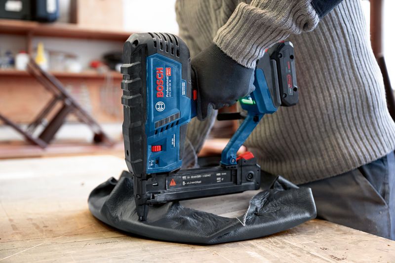 A person wearing safety equipment uses a cordless narrow crown stapler on upholstery.