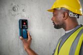 A person wearing safety equipment uses a detector to scan a concrete wall.