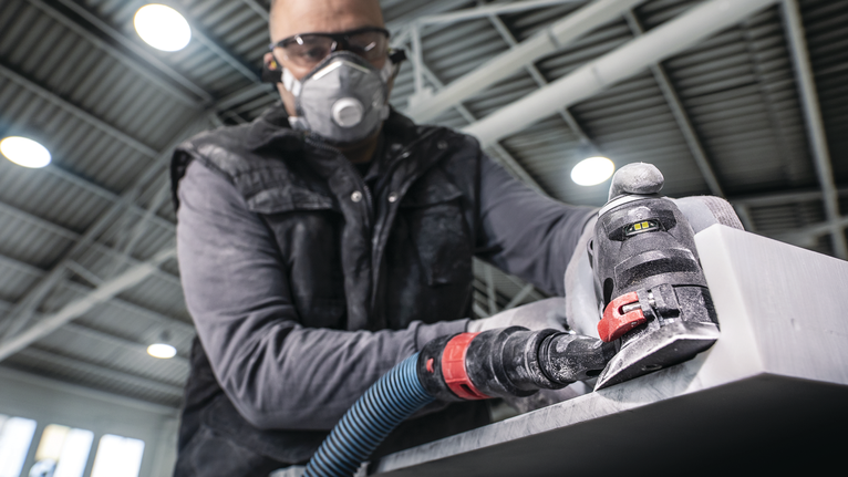 Person wearing safety equipment sands a metal surface with a power tool.