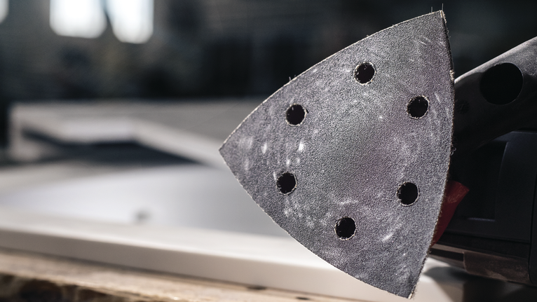 Detail of a delta sander resting on a wooden workbench in a workshop.