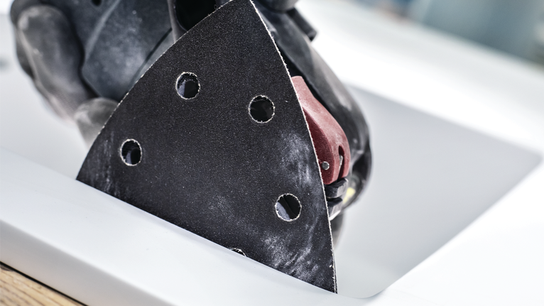 Person wearing safety equipment sanding a countertop with a triangle sander.
