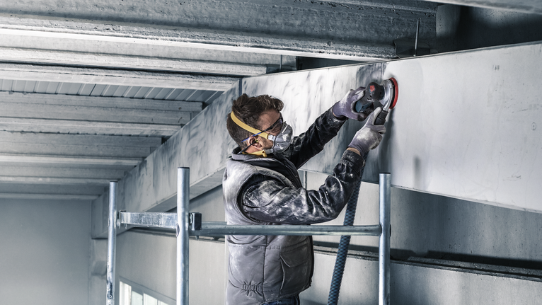 PRO F355 Sanding Disc, 150 mm, G400, 5 pcs A person wearing safety equipment sands a concrete beam using a power tool.